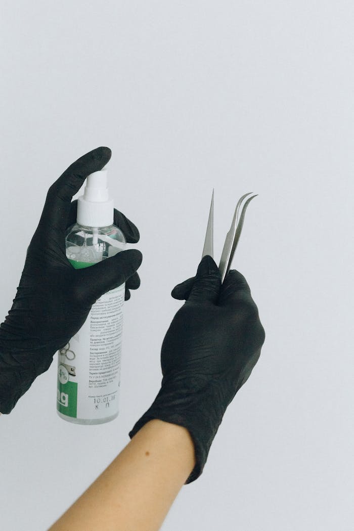 services-02 Black gloved hands holding a medical spray bottle and tweezers on a white background.